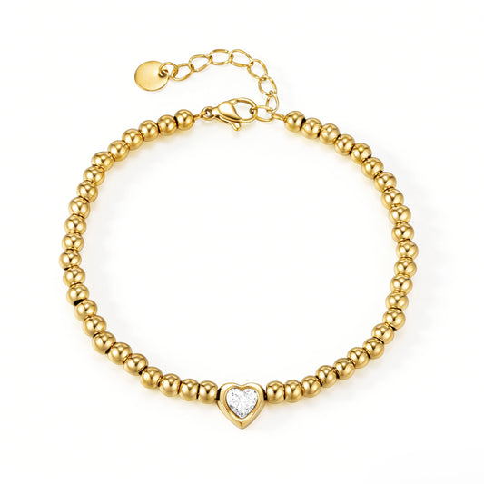 Gold bracelet featuring rounded gold-tone beads and a clear heart-shaped centerpiece, shown on a white background.
