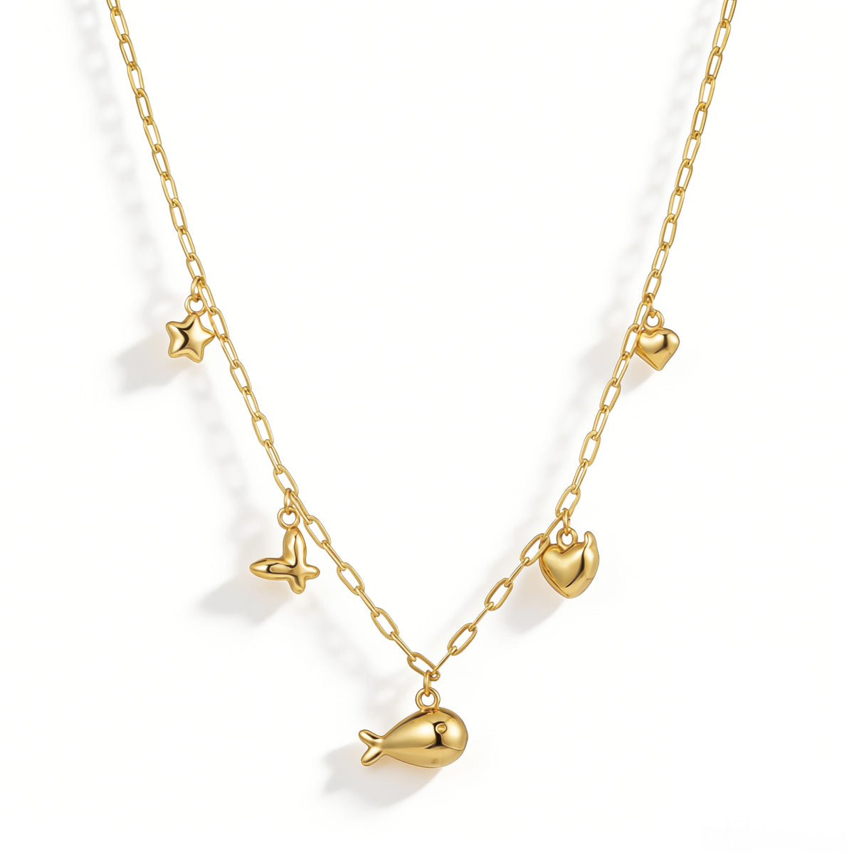 Gold necklace featuring an elongated-link chain with heart, butterfly and planet-shaped charms, shown on a white background.
